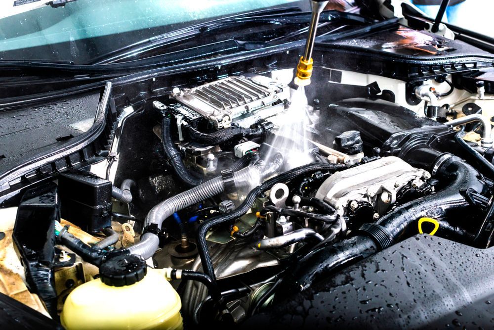 Car engine being cleaned with a pressure washer. Water sprays the engine components.