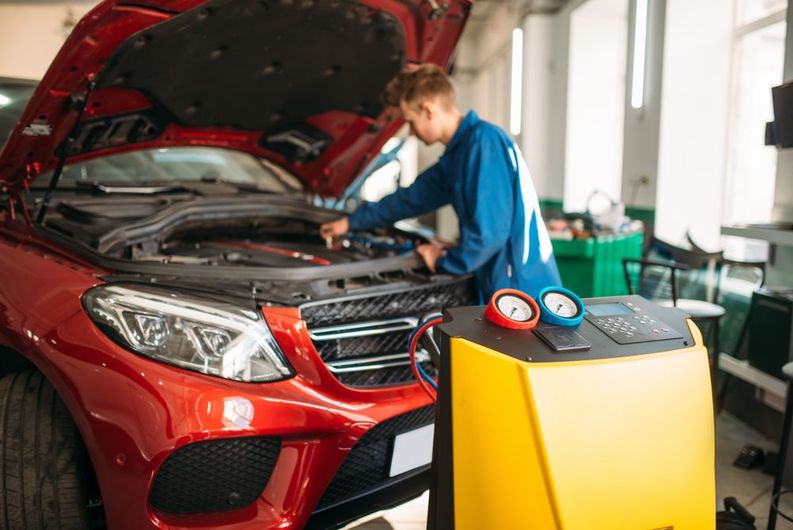 A man is working on the engine of a red car in a garage.