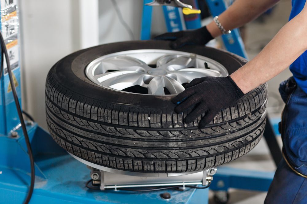 A tire on a machine, being worked on by a person wearing black gloves in a garage setting.