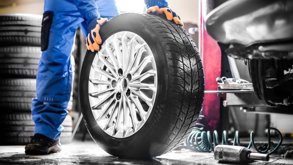 Mechanic in blue overalls holding a tire, garage setting.