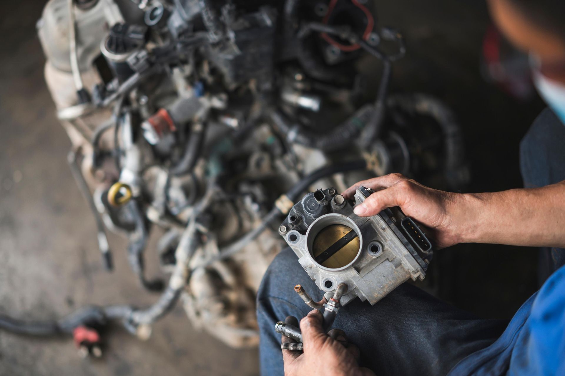 Mechanic working on a car engine, holding a throttle body.