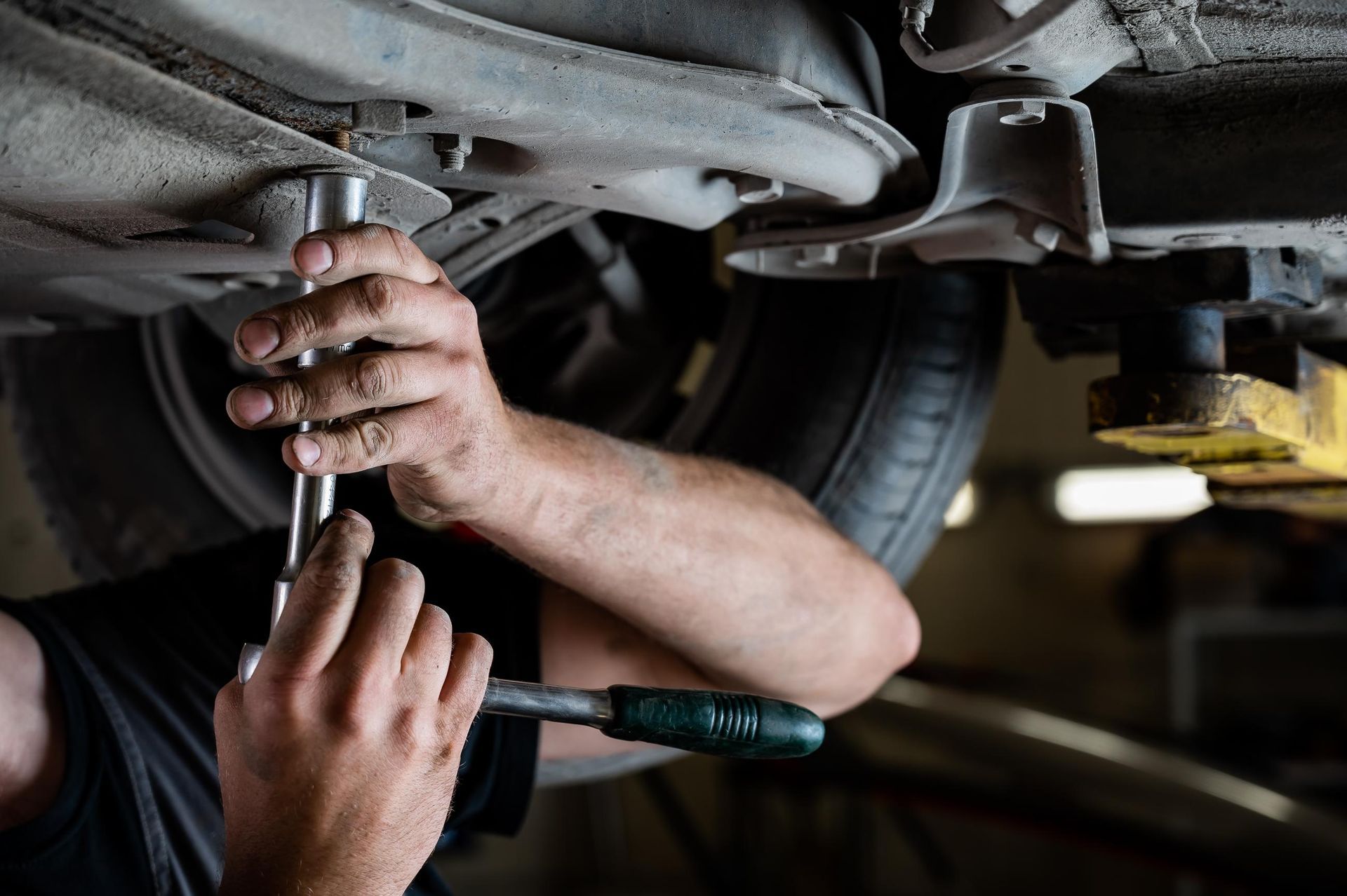 Mechanic working on a car from below, using a wrench.