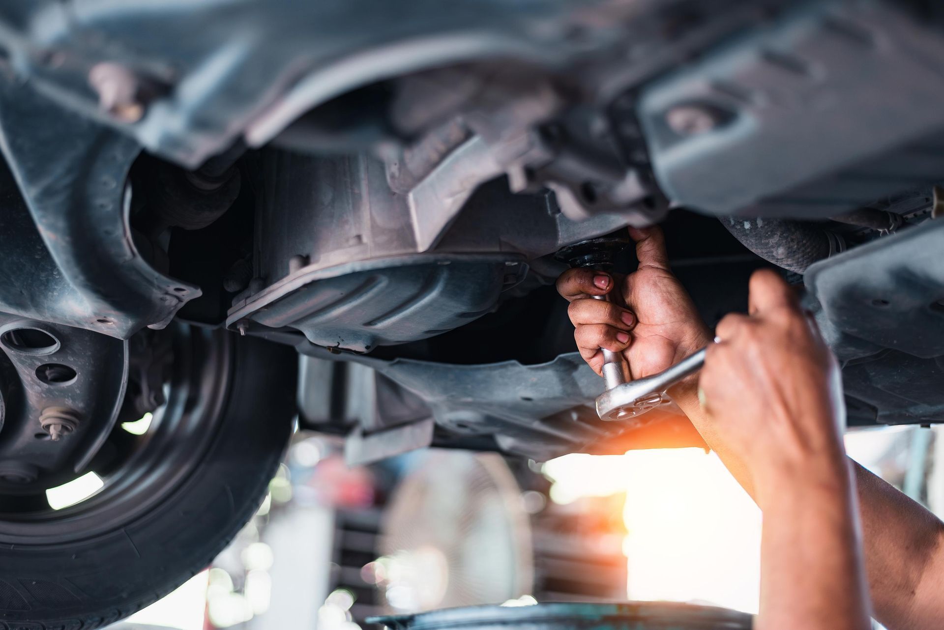 A mechanic uses a ratchet to work on the underside of a car in a garage.