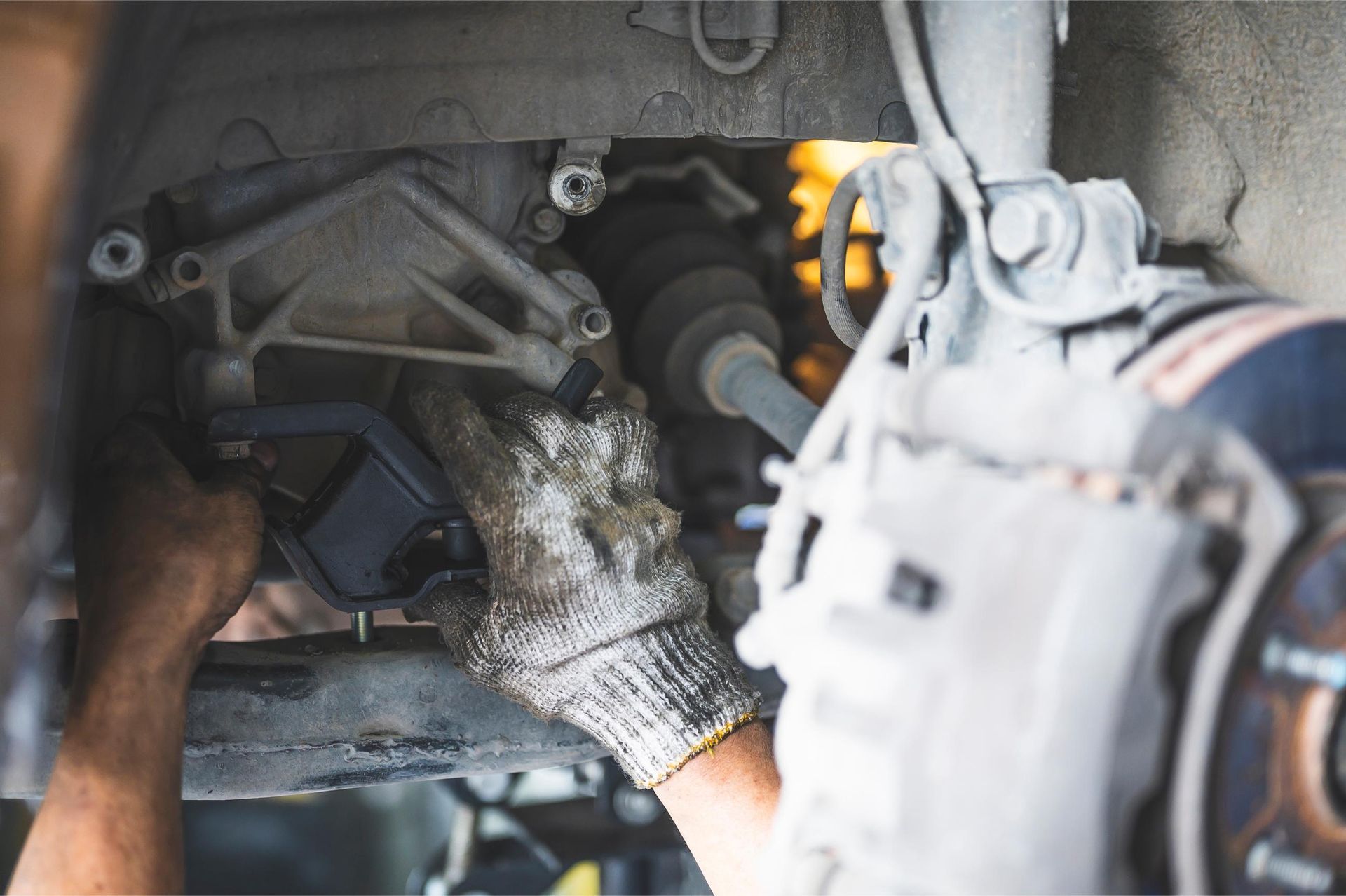 Mechanic working under a car, adjusting suspension near the wheel hub in a garage