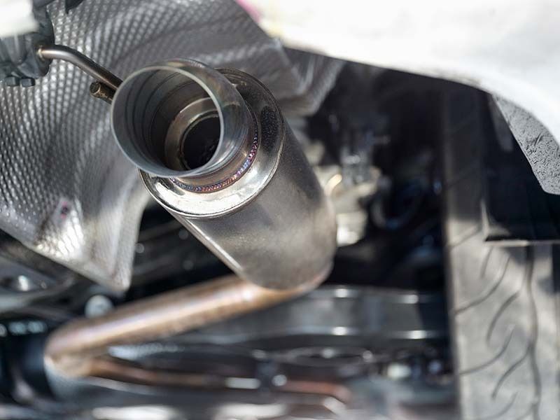 Close-up view of a car exhaust pipe, made of shiny metal, located underneath the vehicle.