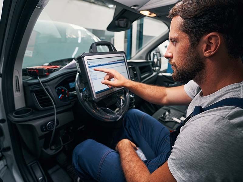 Mechanic using a tablet diagnostic tool inside a vehicle.