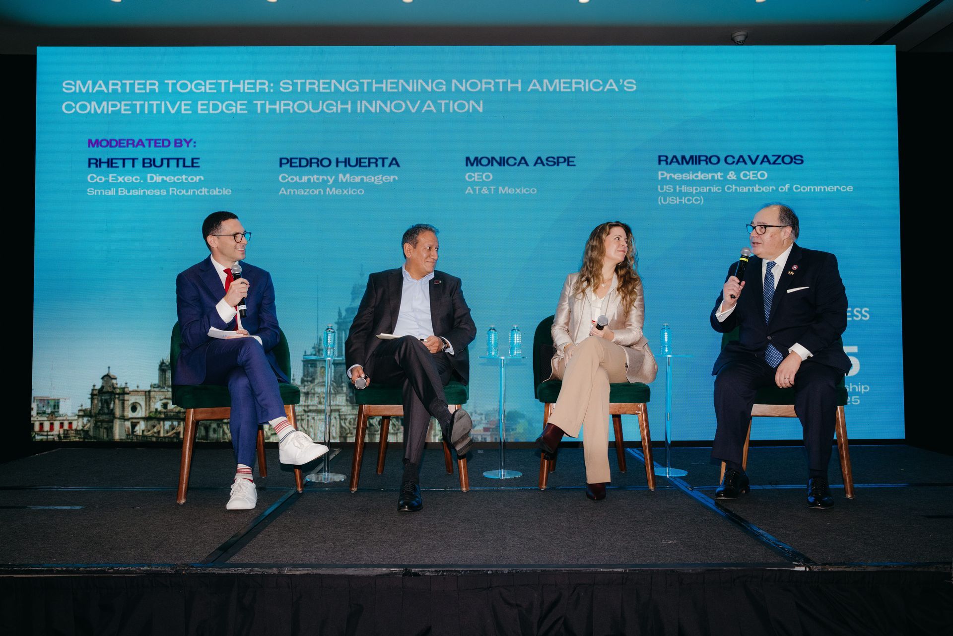 Panel discussion with four people on a stage in front of a screen.