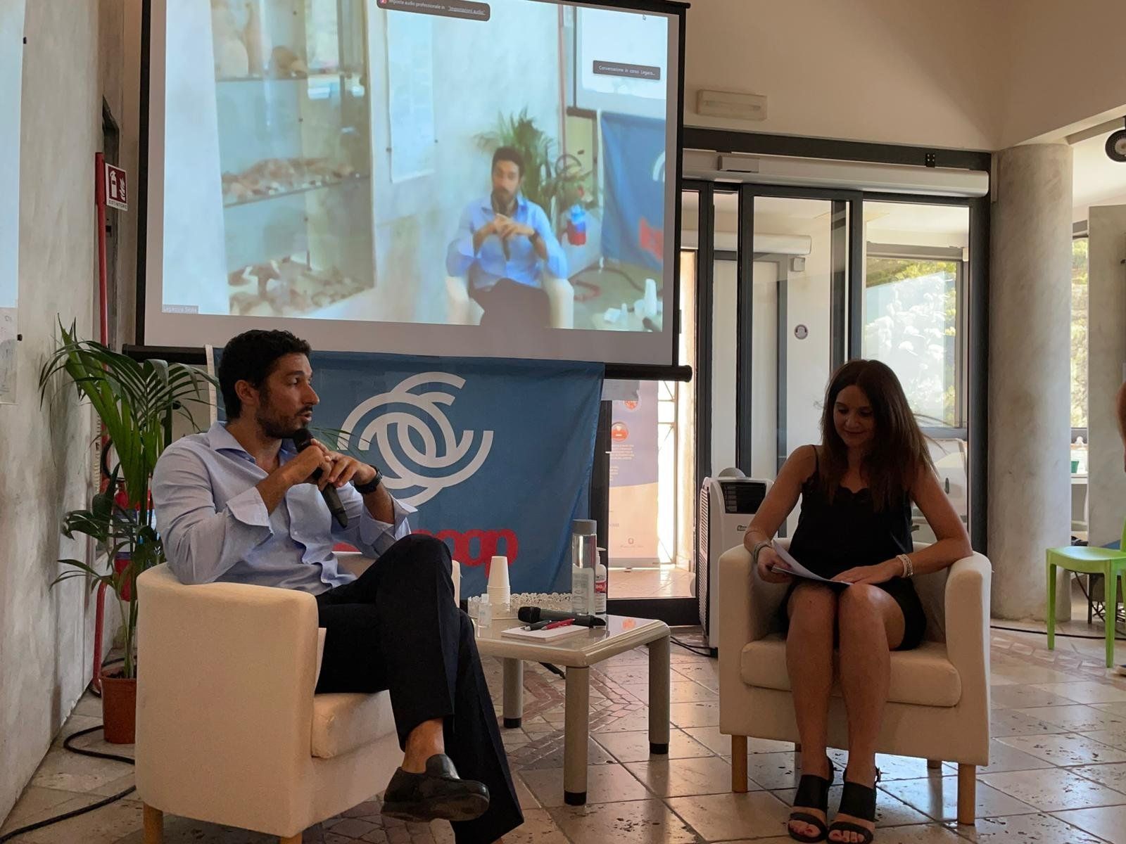 Un uomo e una donna sono seduti su delle sedie davanti allo schermo di un proiettore.