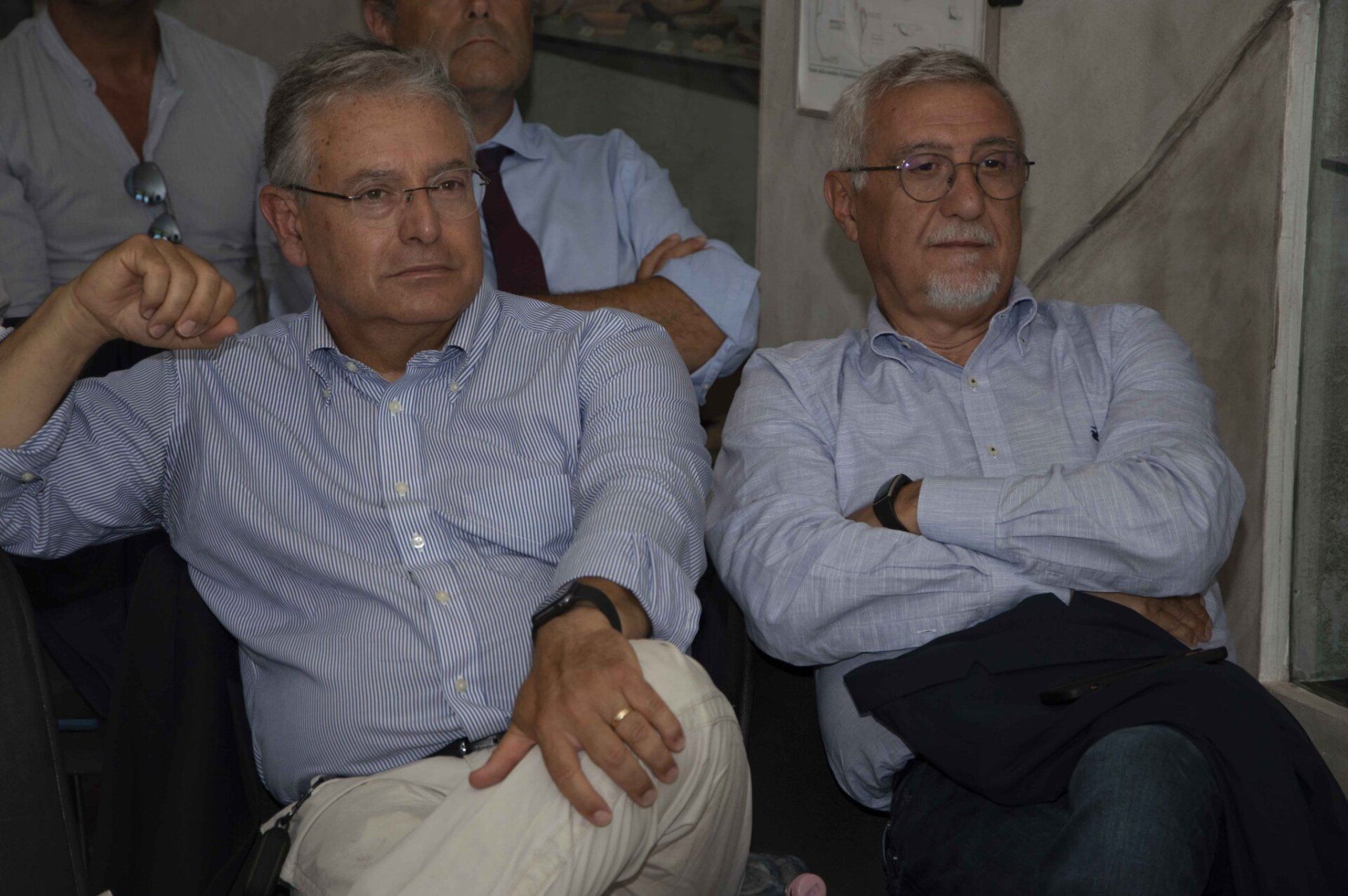 Due uomini sono seduti uno accanto all'altro con le braccia incrociate.