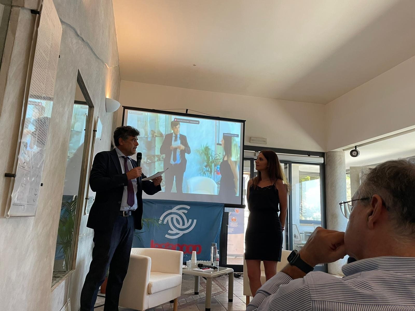 Un uomo e una donna sono in piedi davanti allo schermo di un proiettore.