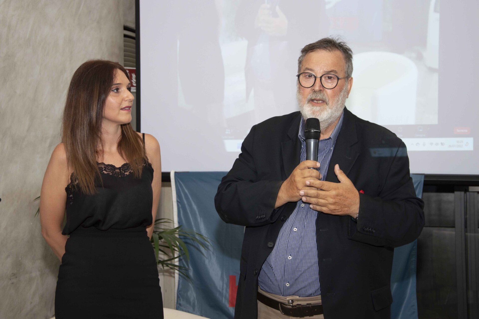 Un uomo con la barba è in piedi accanto a una donna che tiene in mano un microfono.