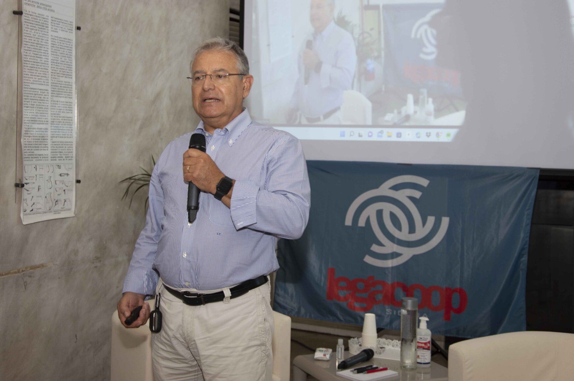 Un uomo è in piedi davanti allo schermo di un proiettore e tiene in mano un microfono.