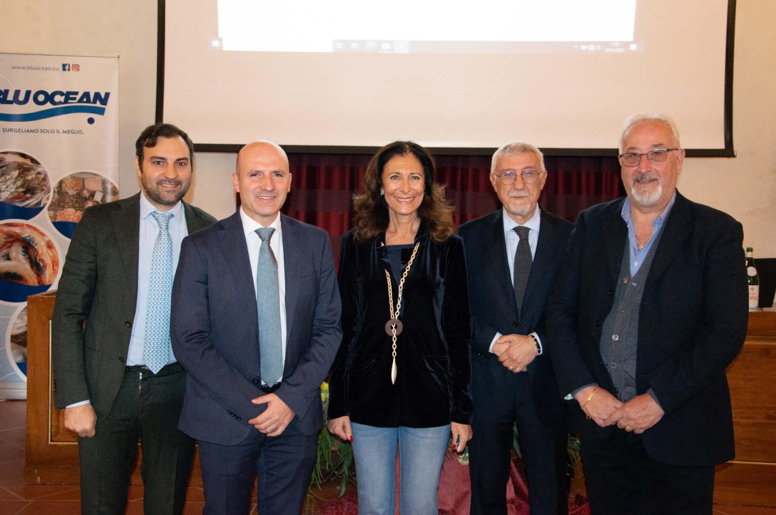 Un gruppo di persone posa per una foto davanti allo schermo di un proiettore.