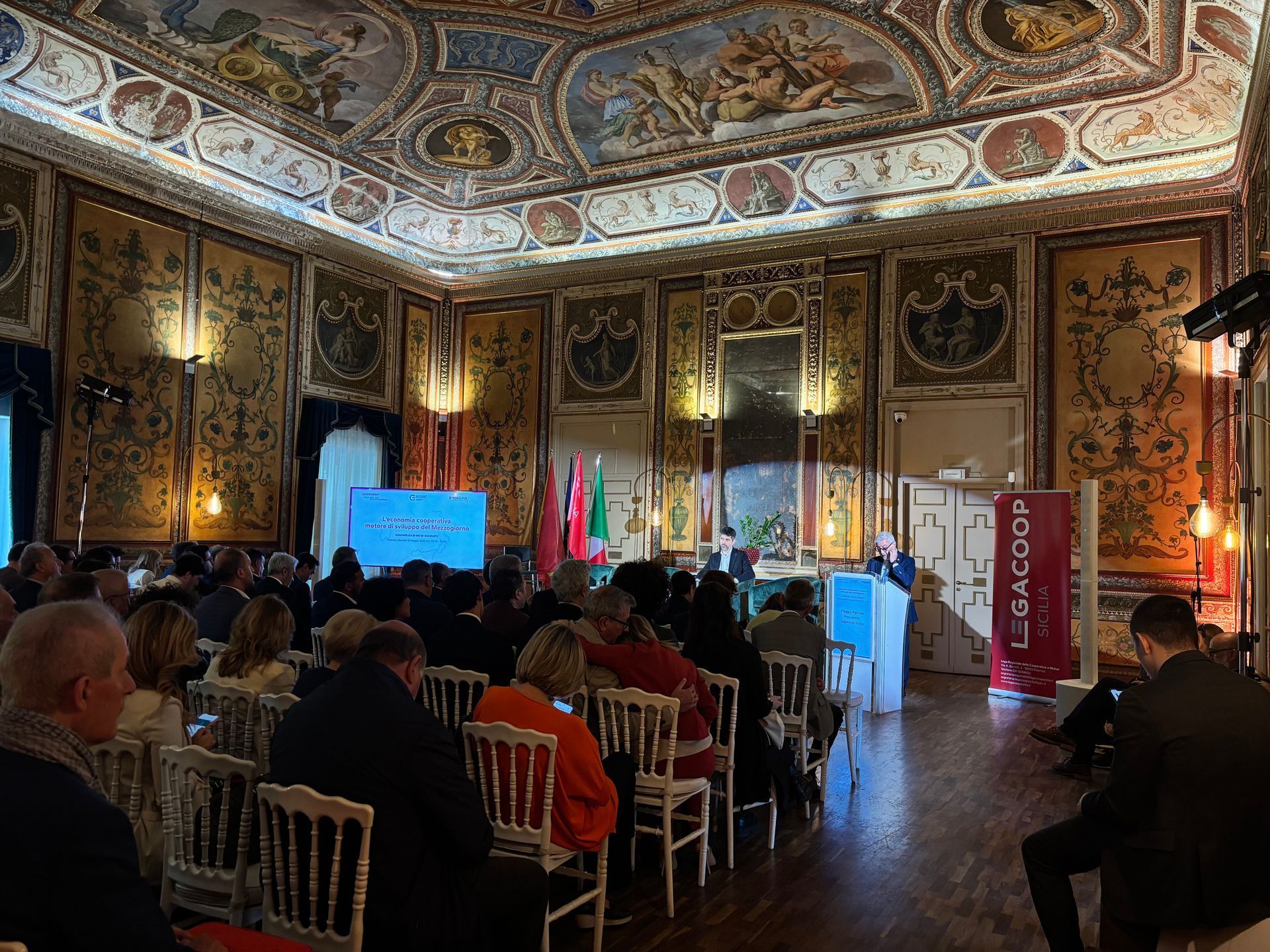 Un gruppo di persone è seduto su delle sedie in una grande stanza.