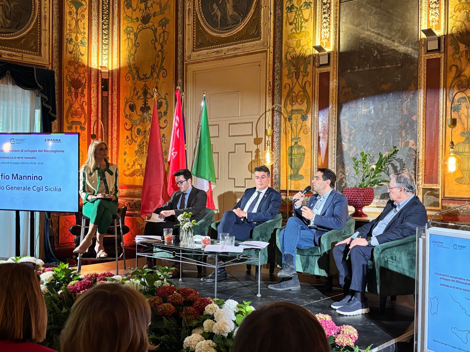 Un gruppo di persone è seduto su delle sedie davanti a un grande schermo in una stanza.