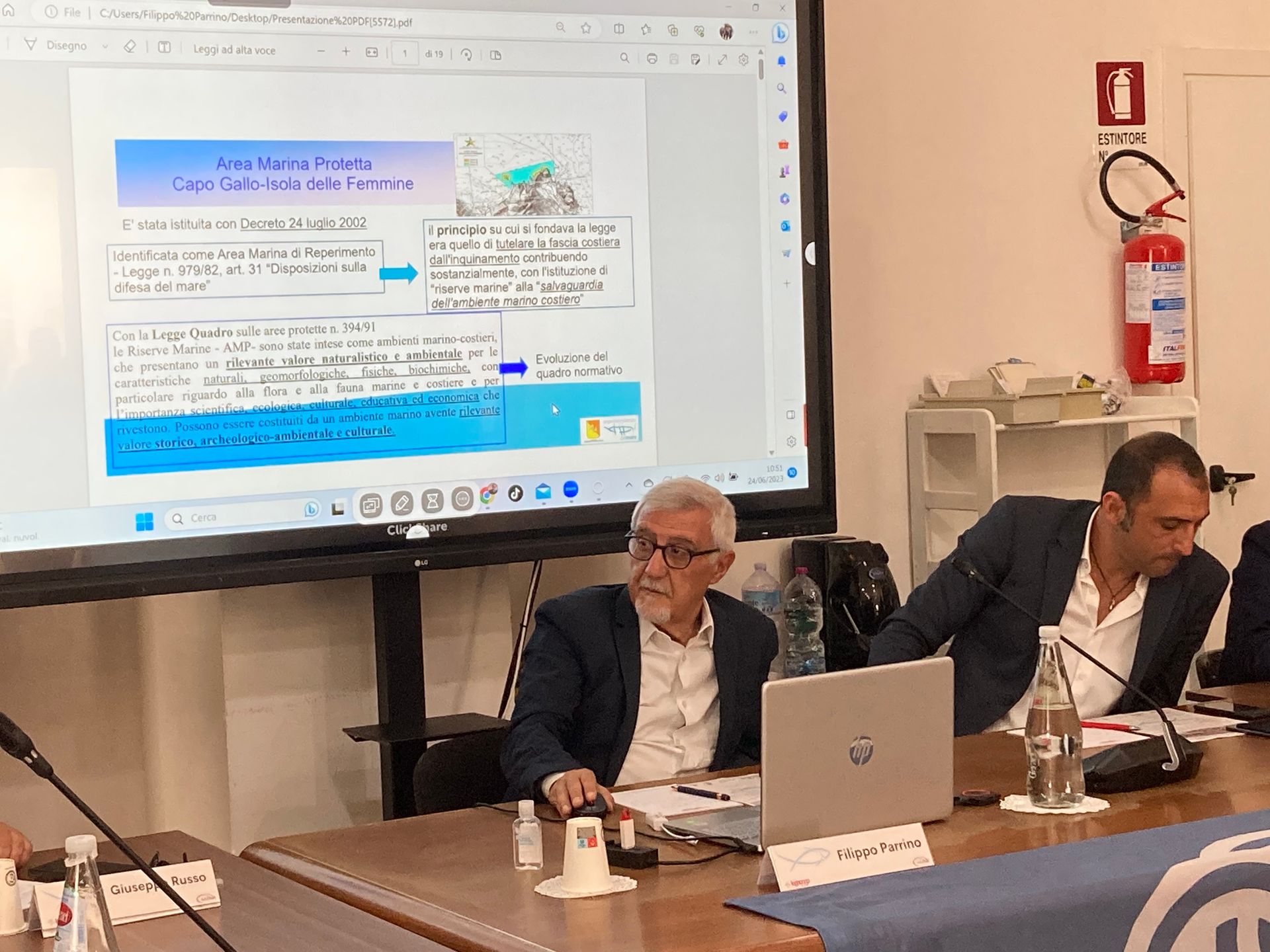 Un uomo è seduto a un tavolo con un computer portatile e uno schermo per proiettore.