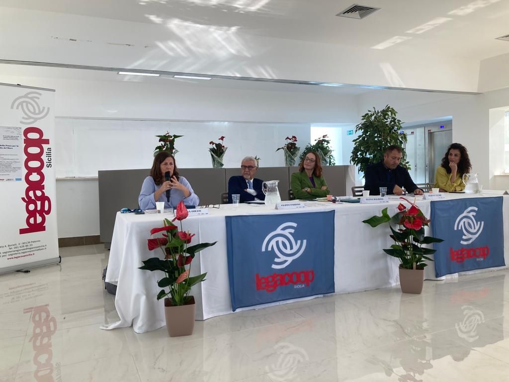 Un gruppo di persone è seduto a un tavolo con un cartello che dice legcoop