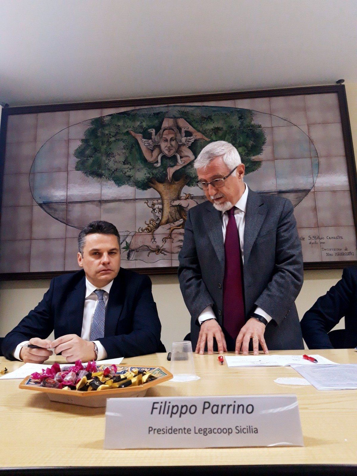 Due uomini sono seduti a un tavolo con un cartello che dice filippo parrino