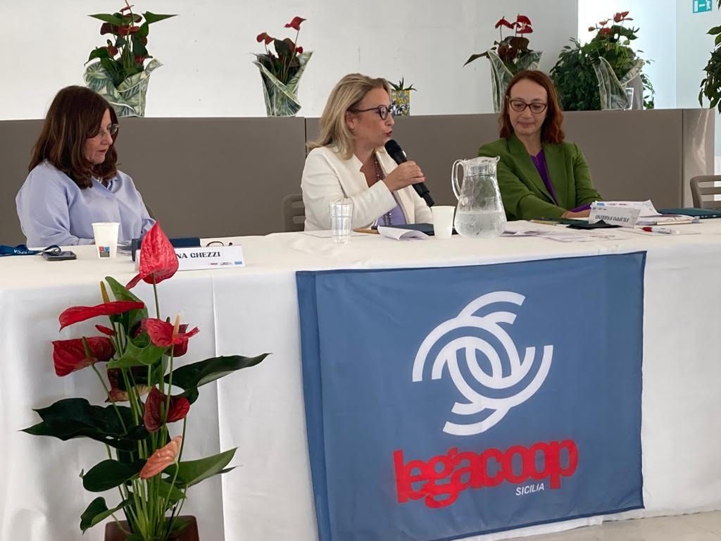 Tre donne sono sedute a un tavolo con una bandiera che dice legacoop