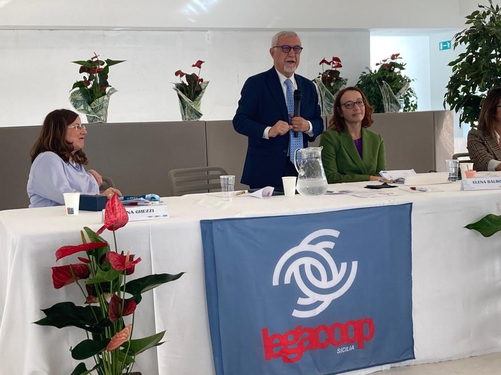 Un uomo in giacca e cravatta è in piedi a un tavolo e parla con un gruppo di persone.