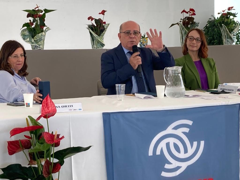 Un uomo parla in un microfono mentre due donne sono sedute a un tavolo