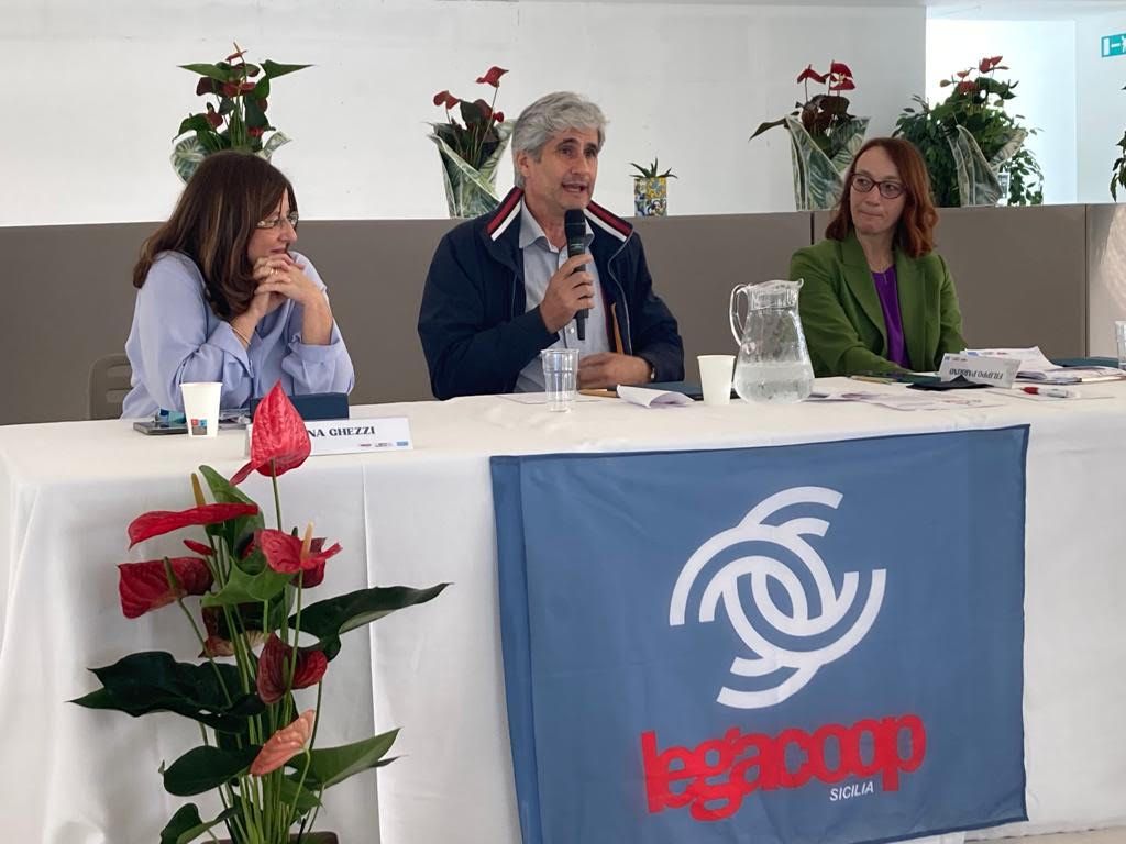 Tre persone sono sedute a un tavolo con una bandiera che dice Legcoop