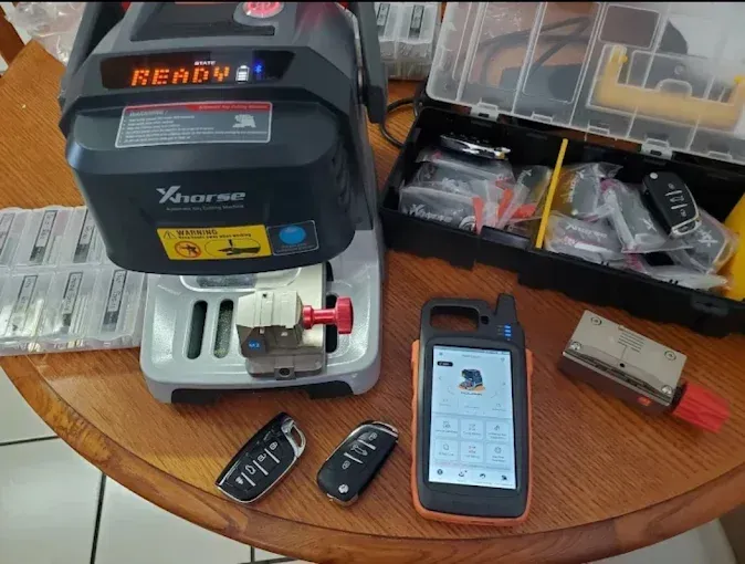A key cutting machine, keys, a remote, and tools on a table, ready for key programming.