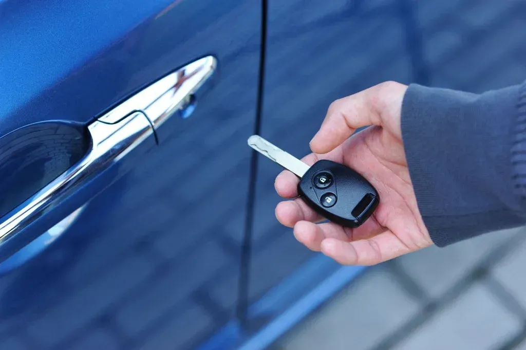 Hand holding car key near blue car door handle.