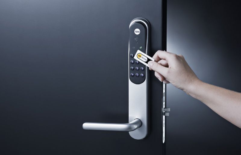 Hand using a key card to unlock a silver and black digital door lock on a dark gray door.