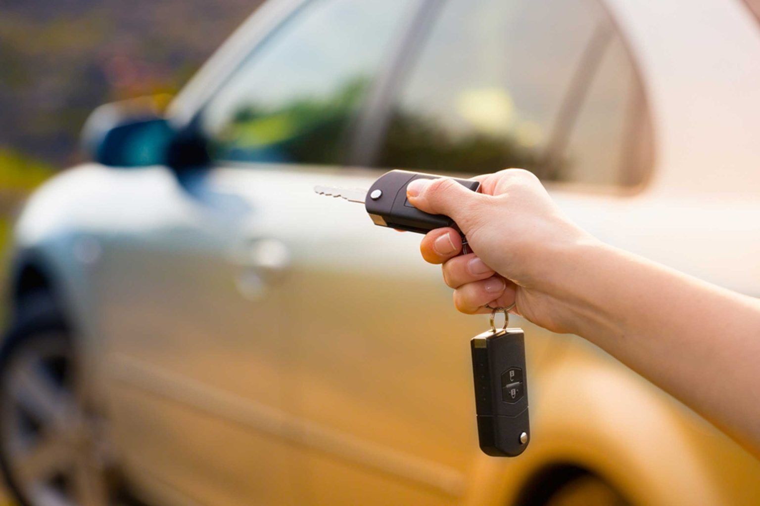 Hand holding car keys in front of a silver car.