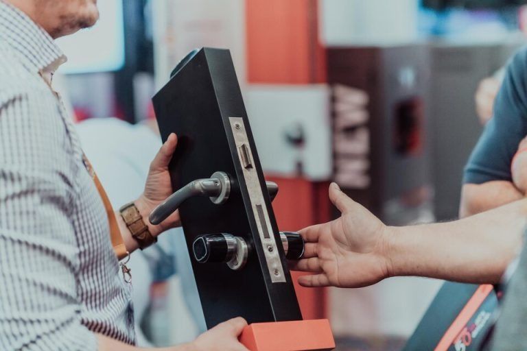 Man demonstrating a black door handle with key, possibly at a trade show.