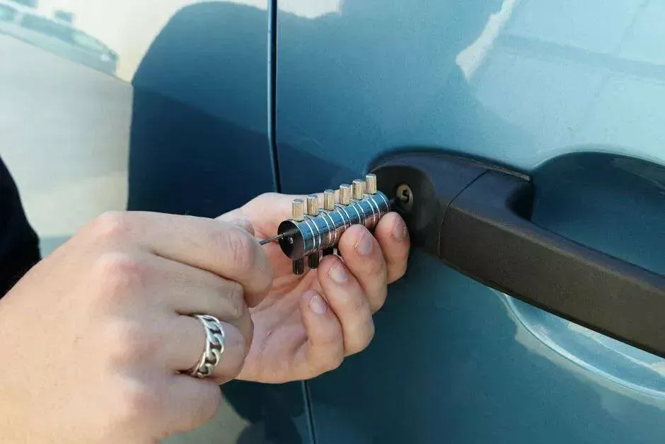 Person using a lock pick to open a teal car door.