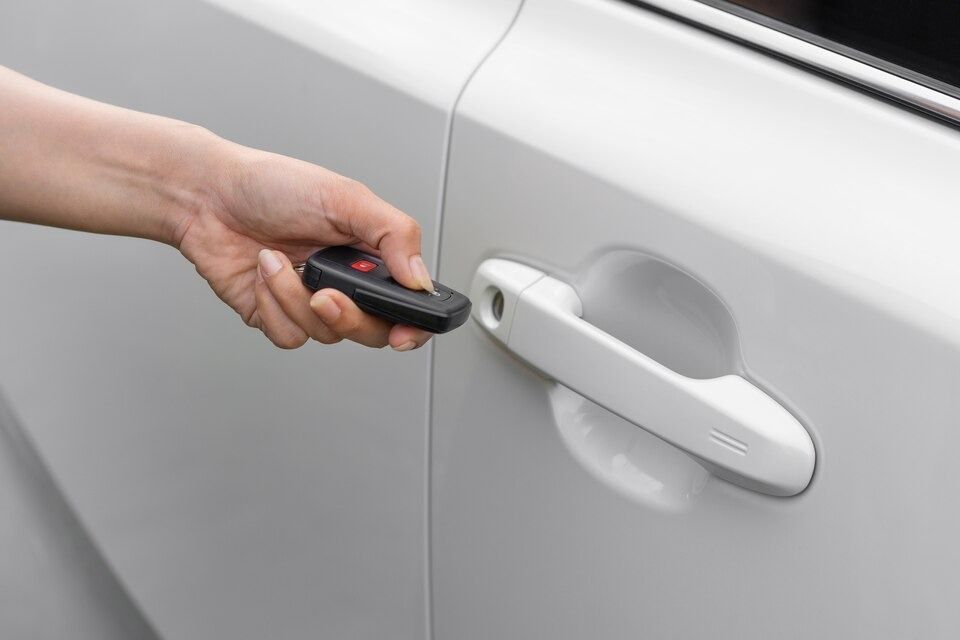 Hand using a car key fob to unlock a white car door.