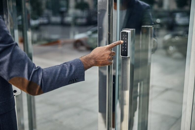 Person in suit entering a building, pressing a keypad on glass door.