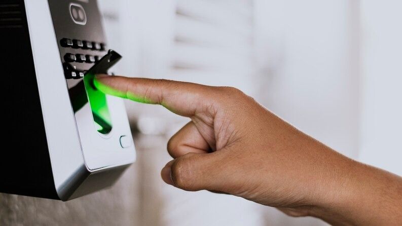 Hand using a fingerprint scanner with a green light.