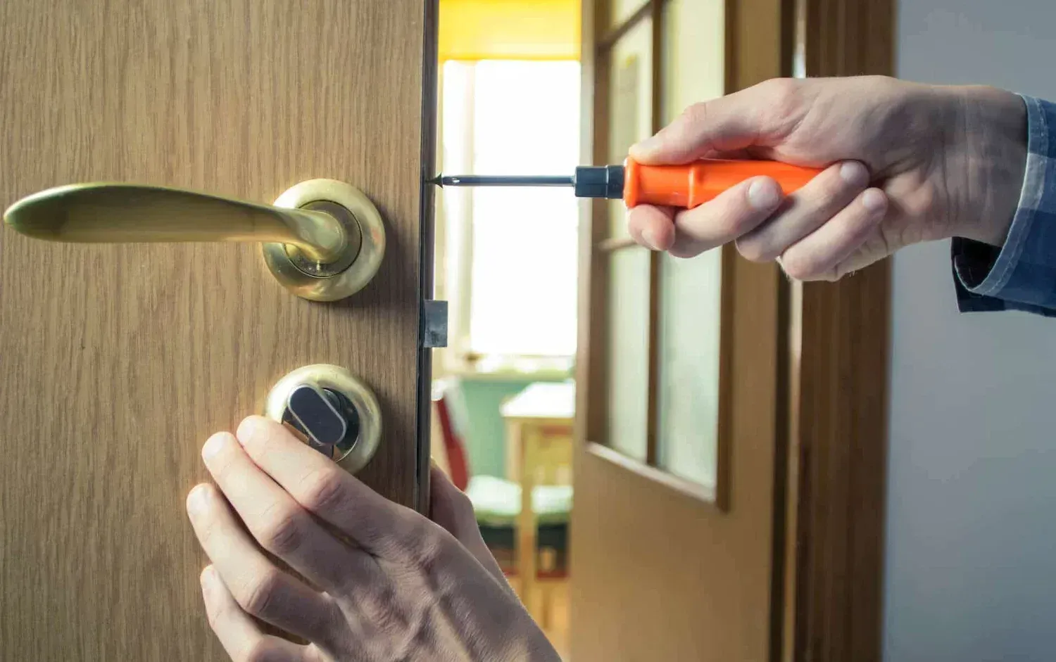 Person using screwdriver to install a door lock on a wooden door.
