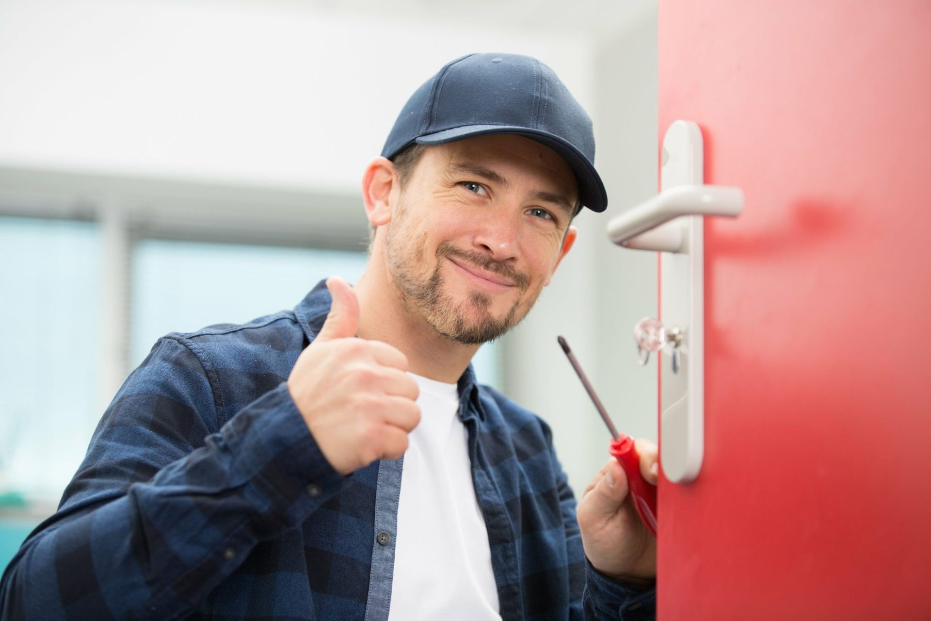 Locksmith giving thumbs up next to a red door, holding a screwdriver.