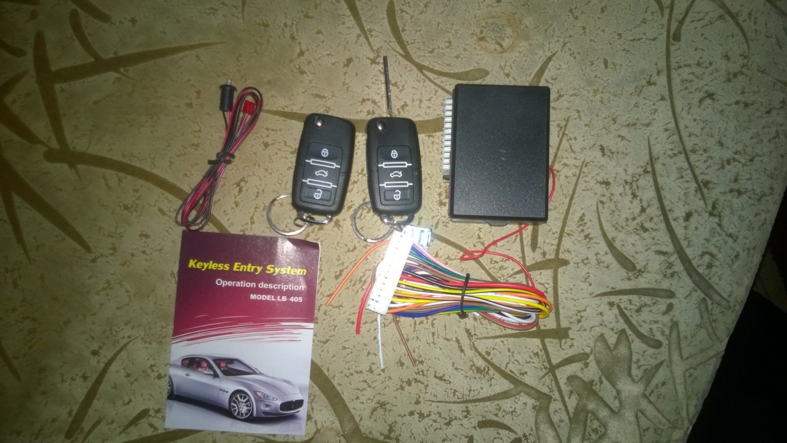 Car alarm system components: two key fobs, control unit, wiring, antenna, and manual.