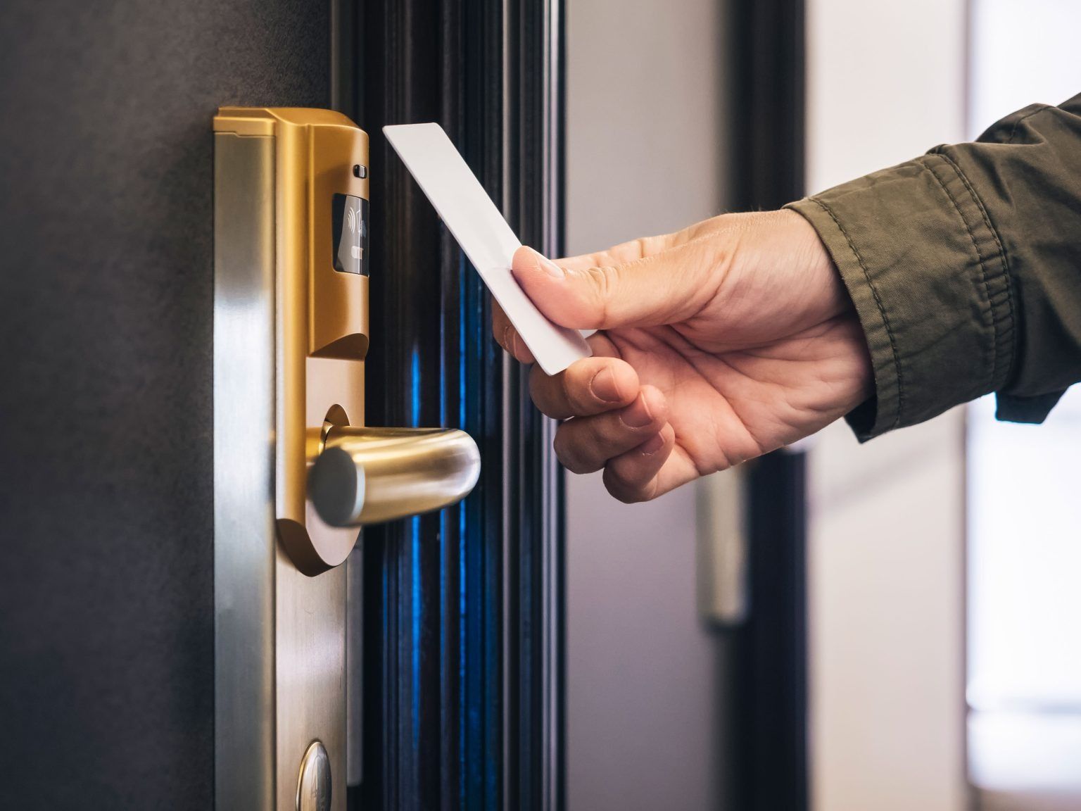 Hand inserting a hotel key card into a gold door lock on a dark door.