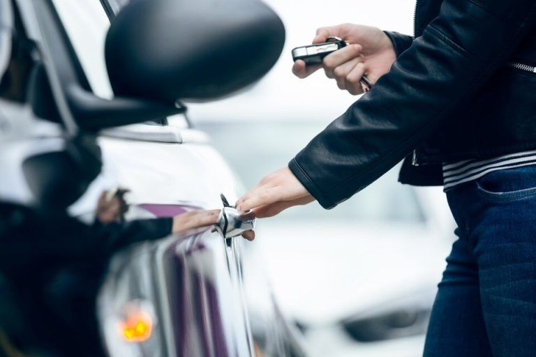 Person opening a car door with a key fob, blurred background.