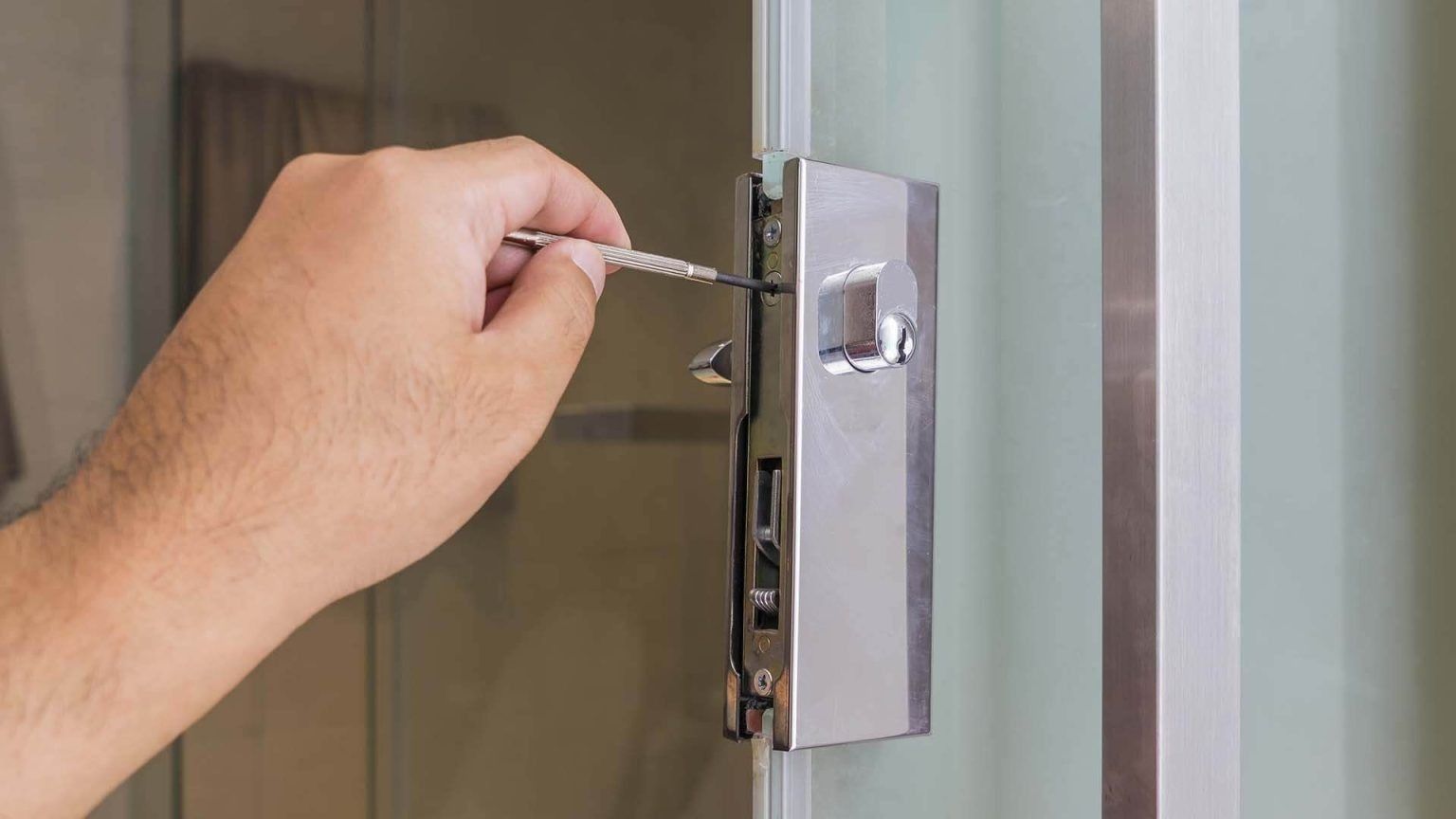 Person using a screwdriver to repair a silver shower door latch.