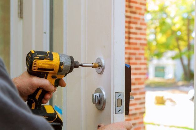 Person using a yellow drill to install a lock on a white door.