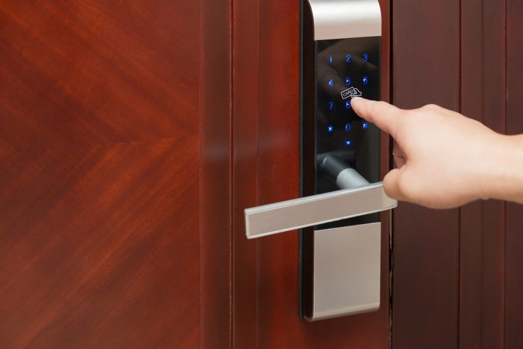 Hand entering code on digital keypad door lock, brown door, silver handle.
