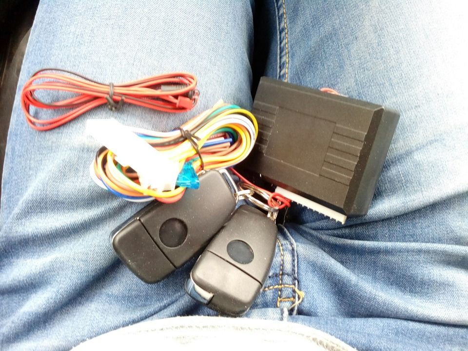 Car remote start system with control unit, wiring, and key fobs on blue jeans.