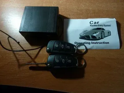 Car remote entry system with black box, two key fobs, and operating instructions on a wooden surface.