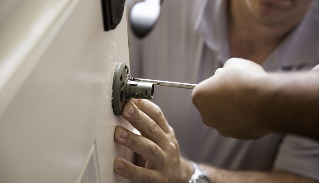 Person installing or repairing a door lock with a screwdriver.
