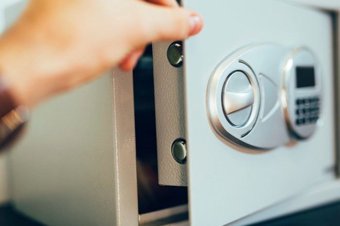 Hand opening a gray safe, revealing the interior.