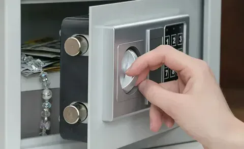 Person opening a small gray safe, revealing jewelry and cash.