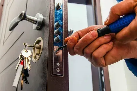 Hand using a screwdriver to fix a door lock, with a key ring hanging nearby.