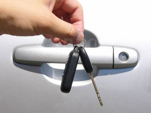 Hand holding car keys near a silver car door handle and lock.